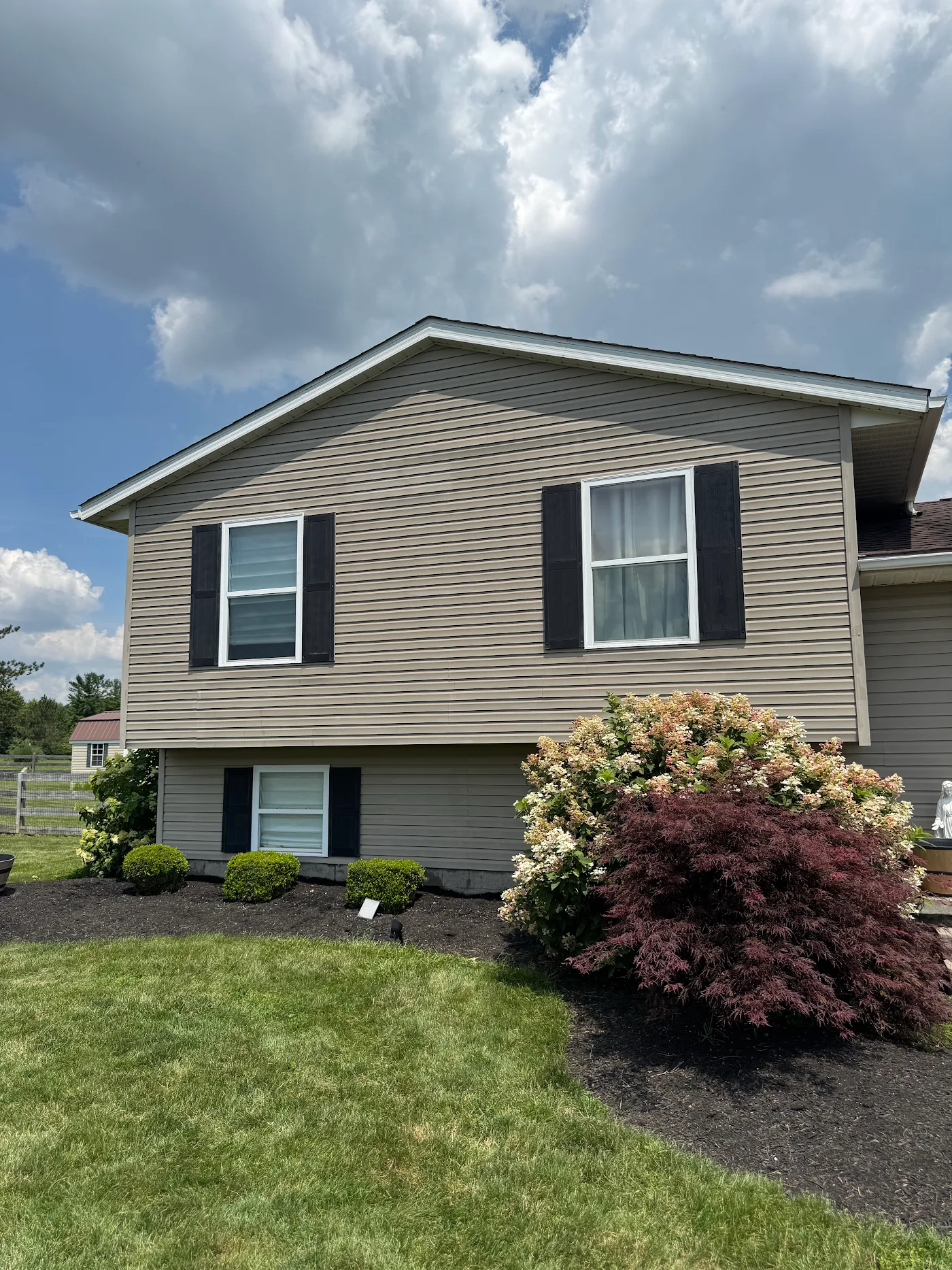 Clean tan vinyl-sided split-level home with black shutters